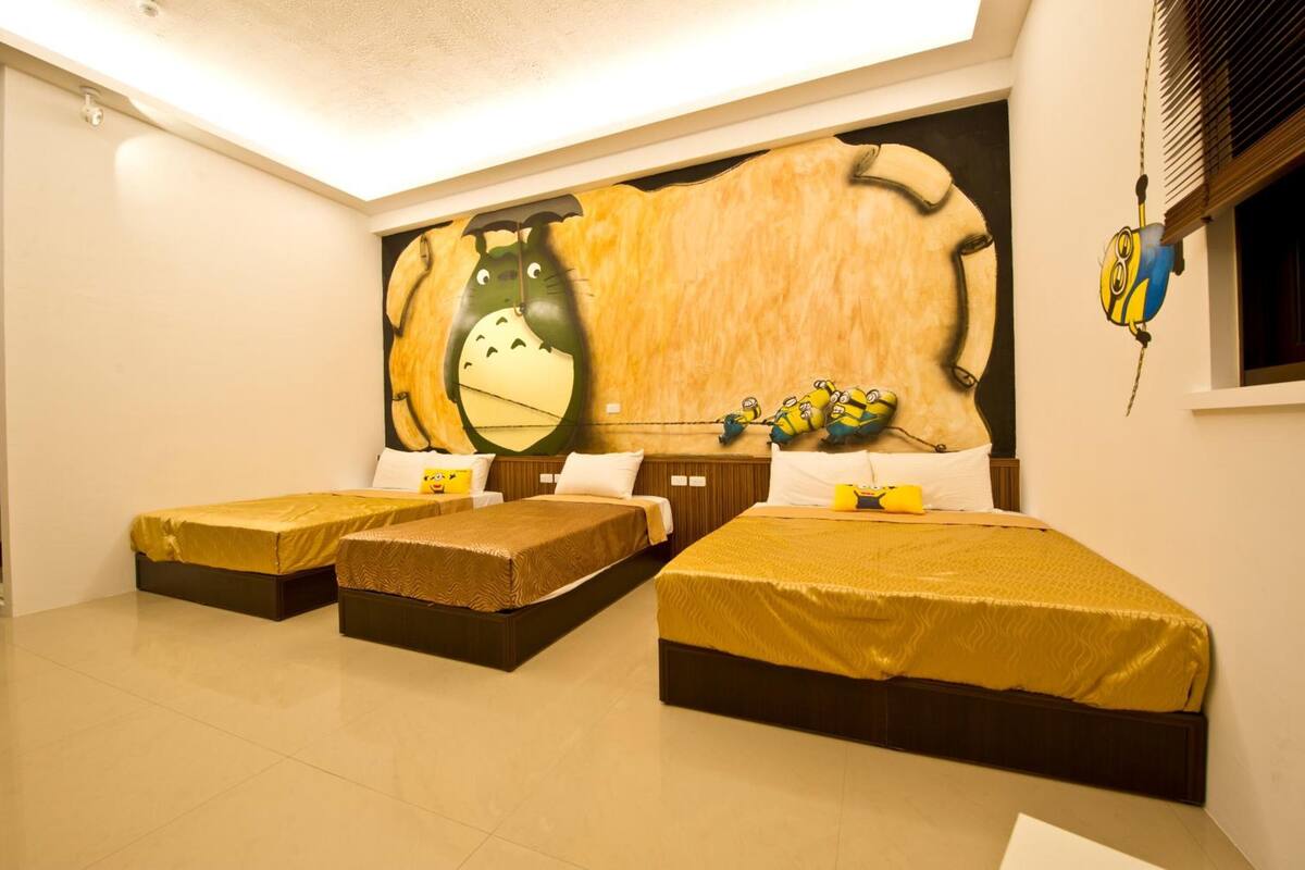 A hotel room with three single beds, a large mural on the wall, and a Minion-themed hanging decoration.