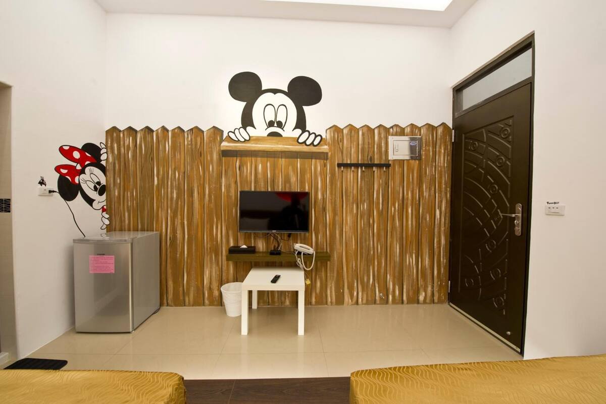 A room with a wooden wall, a television, a small table, a refrigerator, and a door.
