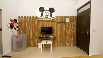A room with a wooden wall, a television, a small table, a refrigerator, and a door.