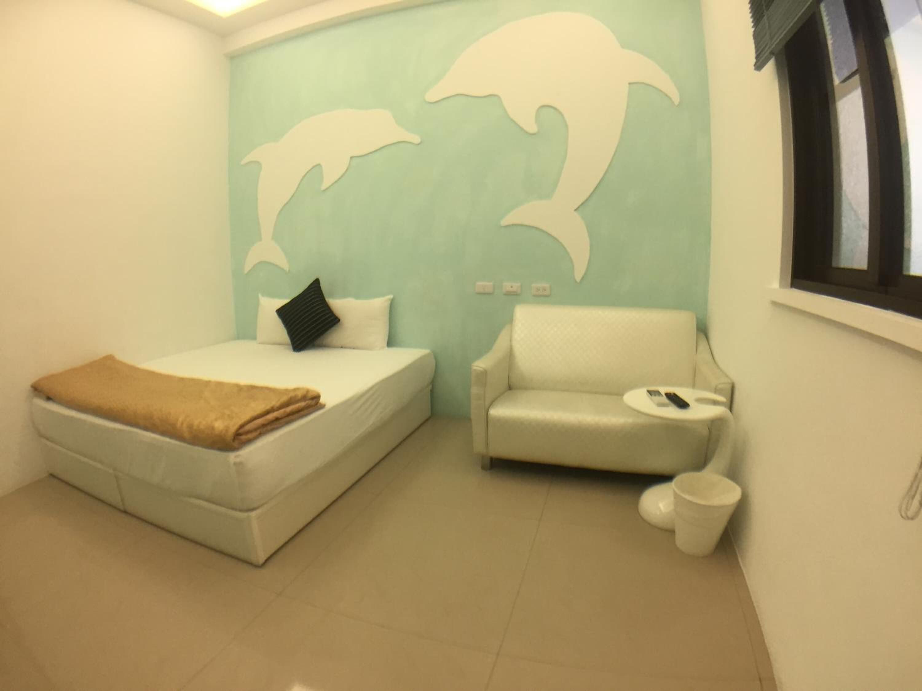 Une pièce comprenant un lit, un canapé, une petite table et un mur décoré de motifs représentant des dauphins.