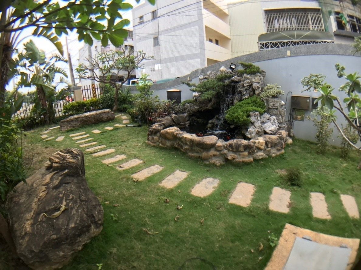 A landscaped garden with a small waterfall, stone pathway, and a large rock.