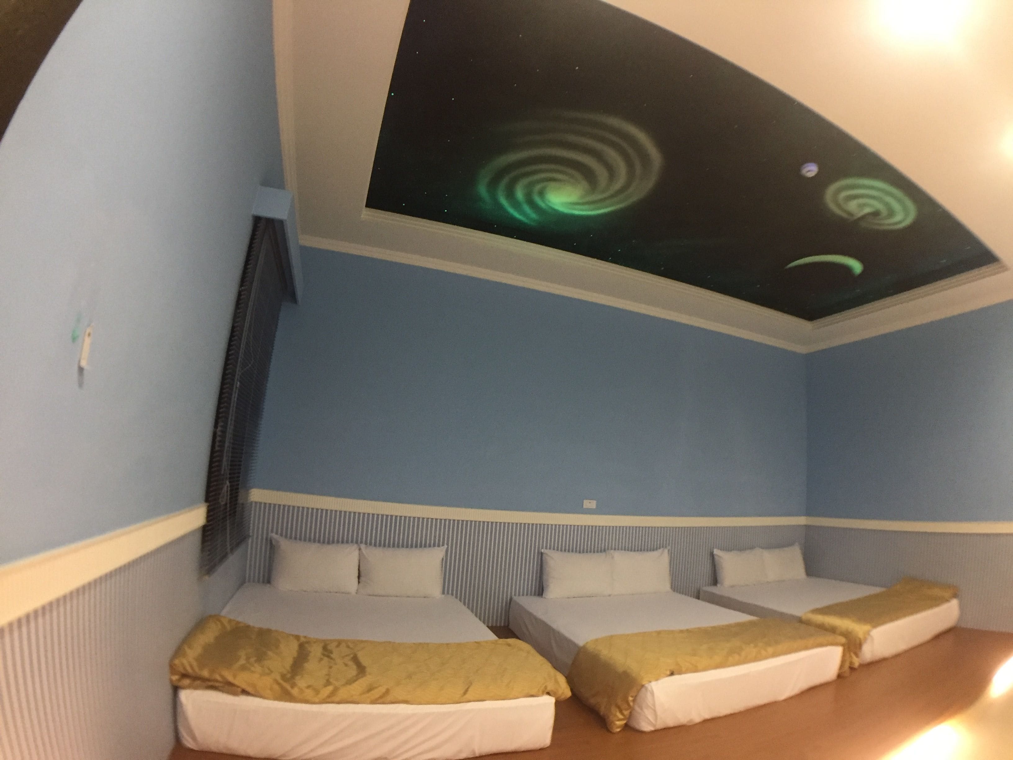 A room with two beds, a ceiling projection of the Northern Lights, and a window with blinds.