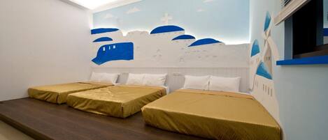 Una habitación con tres camas, un tragaluz y un mural con una escena costera.