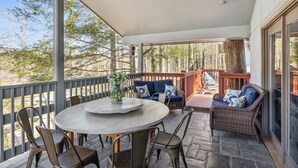 Un patio techado al aire libre con una mesa redonda, sillas, mobiliario de mimbre y vistas a árboles.