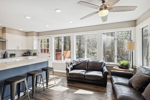 A modern kitchen with a central island, bar stools, a leather sofa, and a ceiling fan. - Downtown Cabin w/Ball Court, Hot Tub, & Firepit (GATLINBURG)