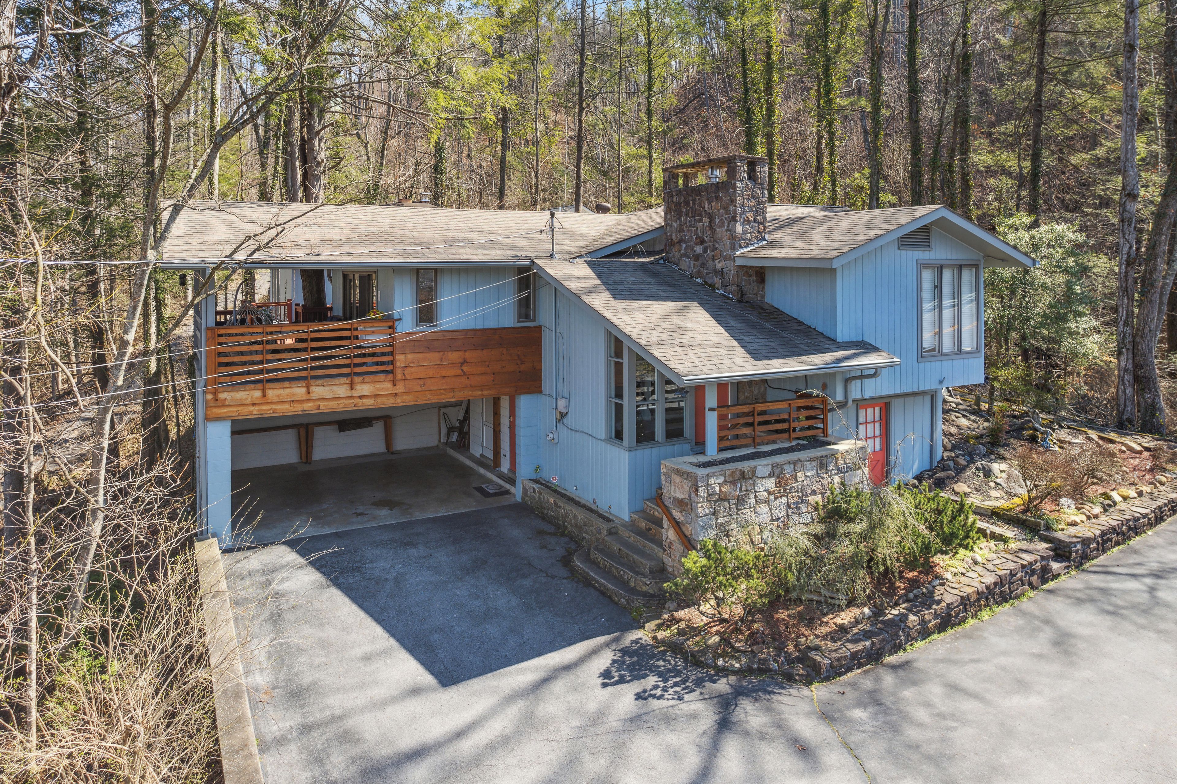 A two-story house with a stone chimney, a wooden deck, and a garage.