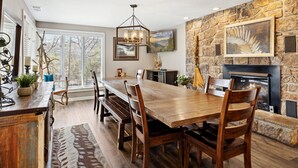 Un comedor amplio con una larga mesa de madera, bancos y una pared de piedra con chimenea.