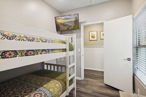 A bunk bed room with patterned bedding, a television on the wall, and a door leading to another room. - Downtown Cabin w/Ball Court, Hot Tub, & Firepit (GATLINBURG)