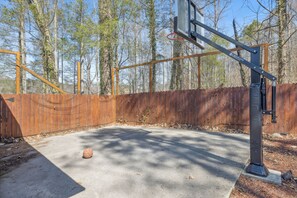 Una cancha de baloncesto al aire libre con valla de madera y árboles al fondo.