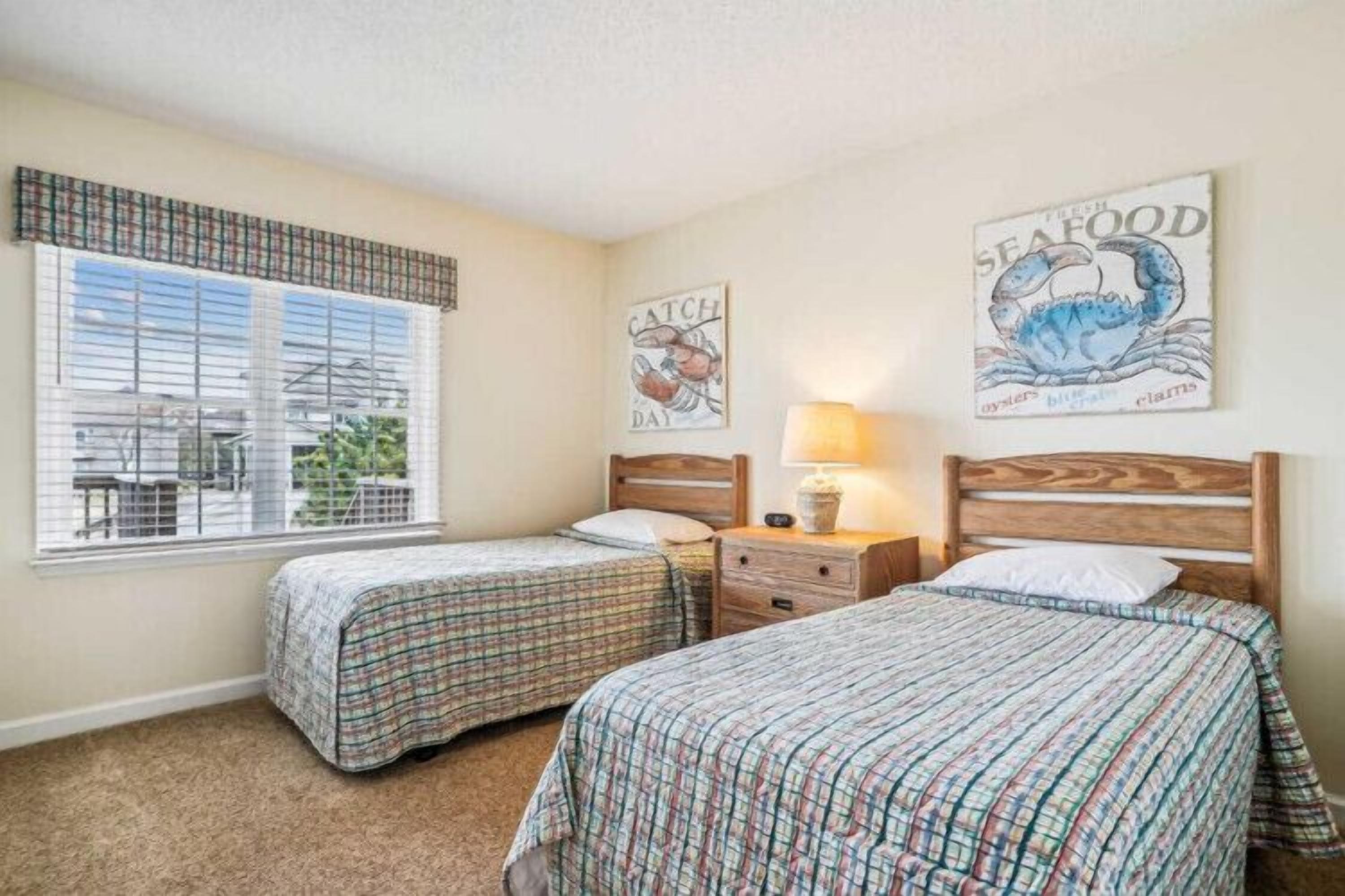 A bedroom with two beds, a window with blinds, and wall art.