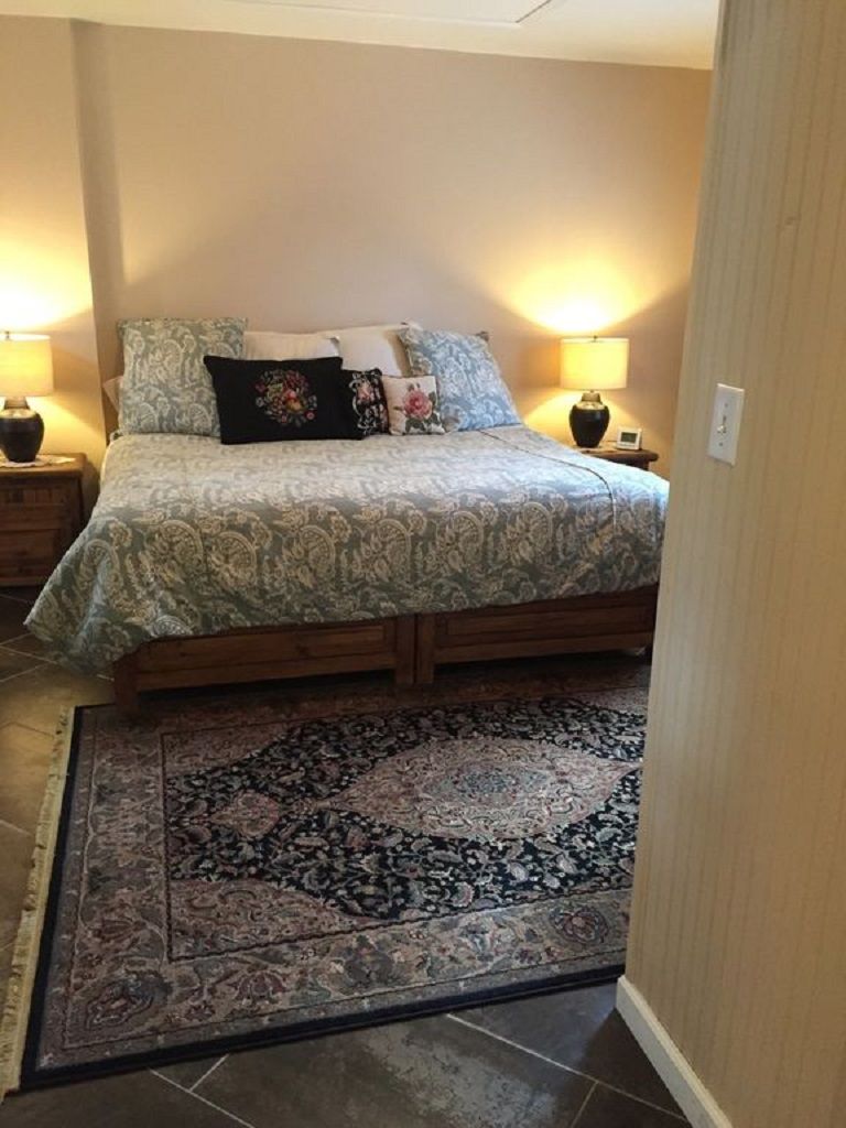 Un dormitorio con una cama, dos lámparas de noche, un tapete y una mesita de noche.