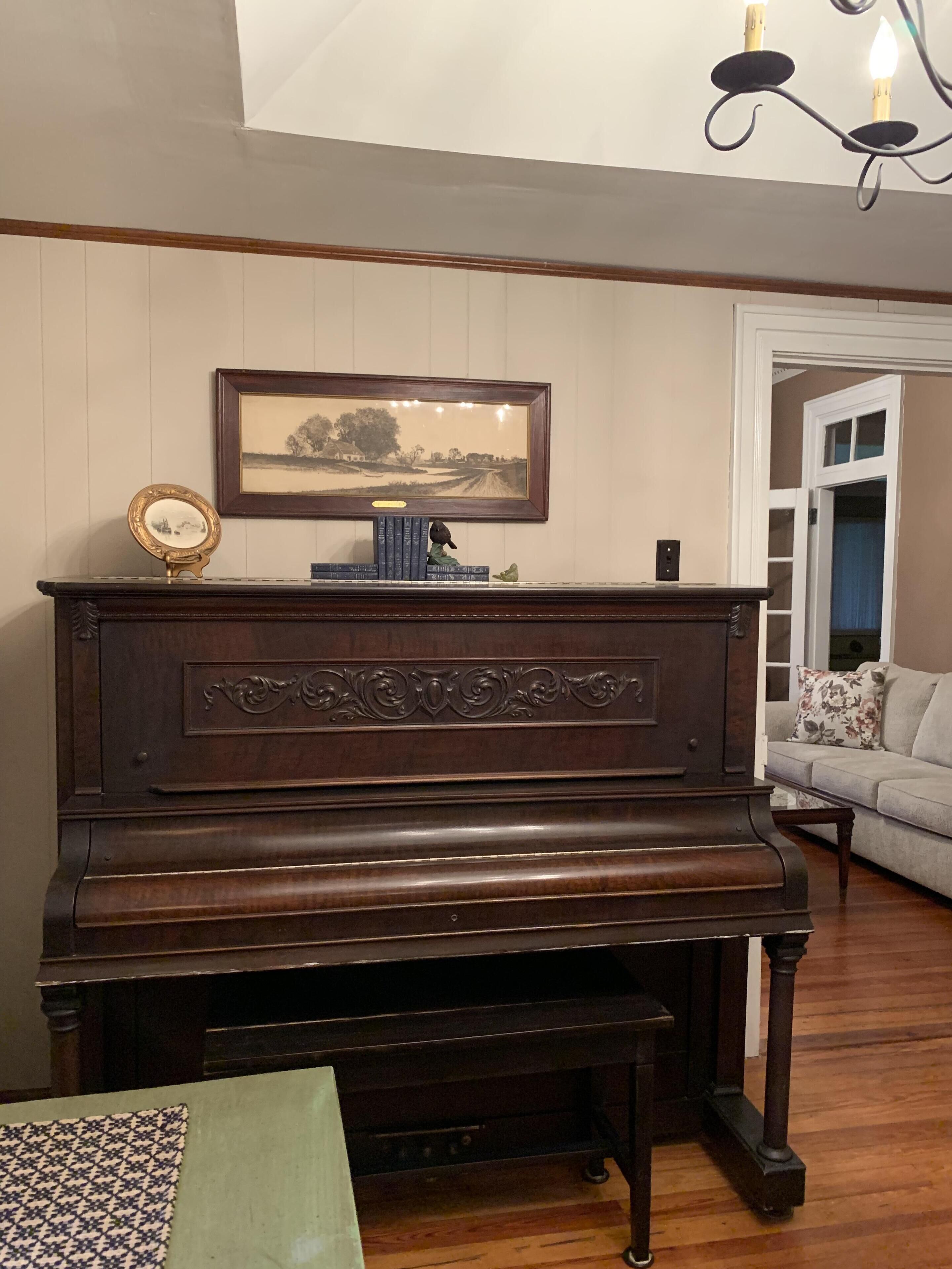 A grand piano in a room with wooden paneling, a framed landscape painting, and a small decorative frog statue.