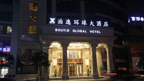Das Außere des Boutix Global Hotels mit beleuchteter Beschilderung, großen Säulen und einem gut beleuchteten Eingang.