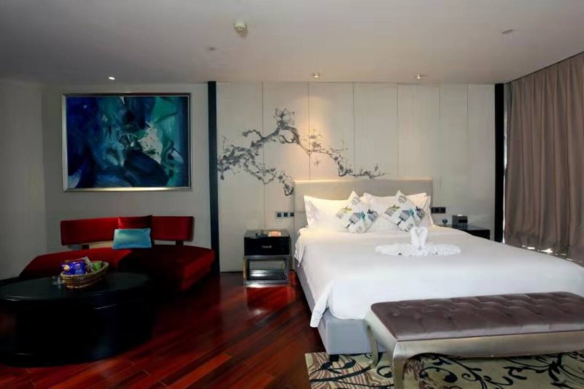 Ein modernes Hotelzimmer mit einem großen Bett, einem roten Sofa, einem kleinen runden Tisch und einem großen, abstrakten Gemälde an der Wand.