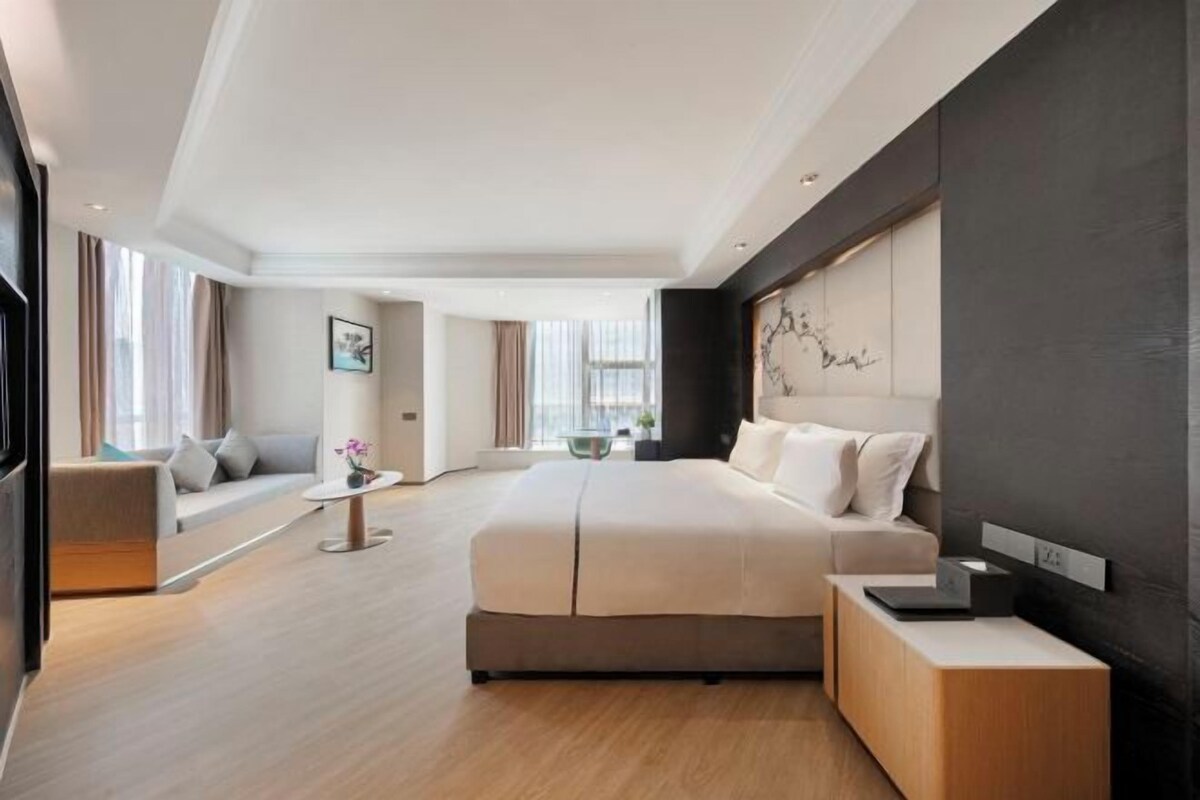 Habitació d'hotel moderna amb un llit gran, una taula de nit, un sofà i vistes a la ciutat.
