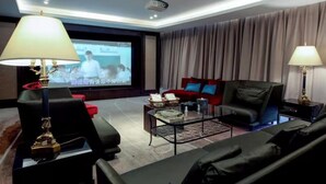 Ein modernes Wohnzimmer mit einem großen Bildschirm, schwarzen Ledersofas, einem Couchtisch und zwei Lampen.