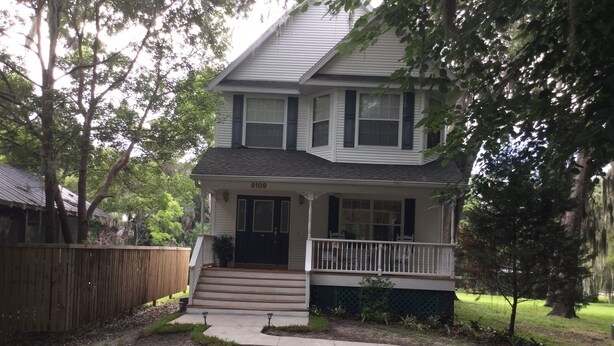 A two-story house with a front porch, a number 6109 on the door, and a fenced yard.