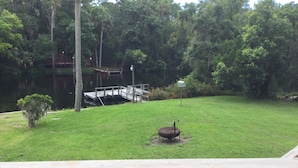 A grassy yard with a wooden deck, a small pond, and a bird feeder.