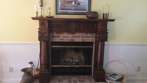 A fireplace with a framed picture above it, a candle holder, and a basket with books beside it.