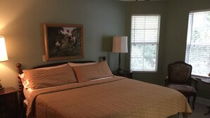 A bedroom with a large bed, a nightstand, a chair, and a window with blinds.