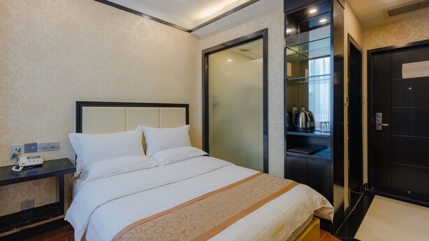 A hotel room with a bed, a nightstand with a phone and a lamp, a wardrobe, and a door with a note on it.