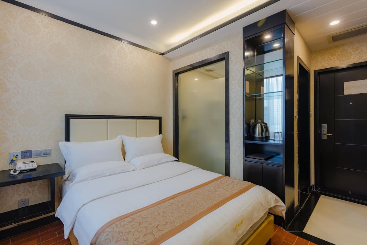 Ein Hotelzimmer mit Bett, Nachttisch mit Telefon und Lampe, Schrank und einer Tür mit einem Zettel.