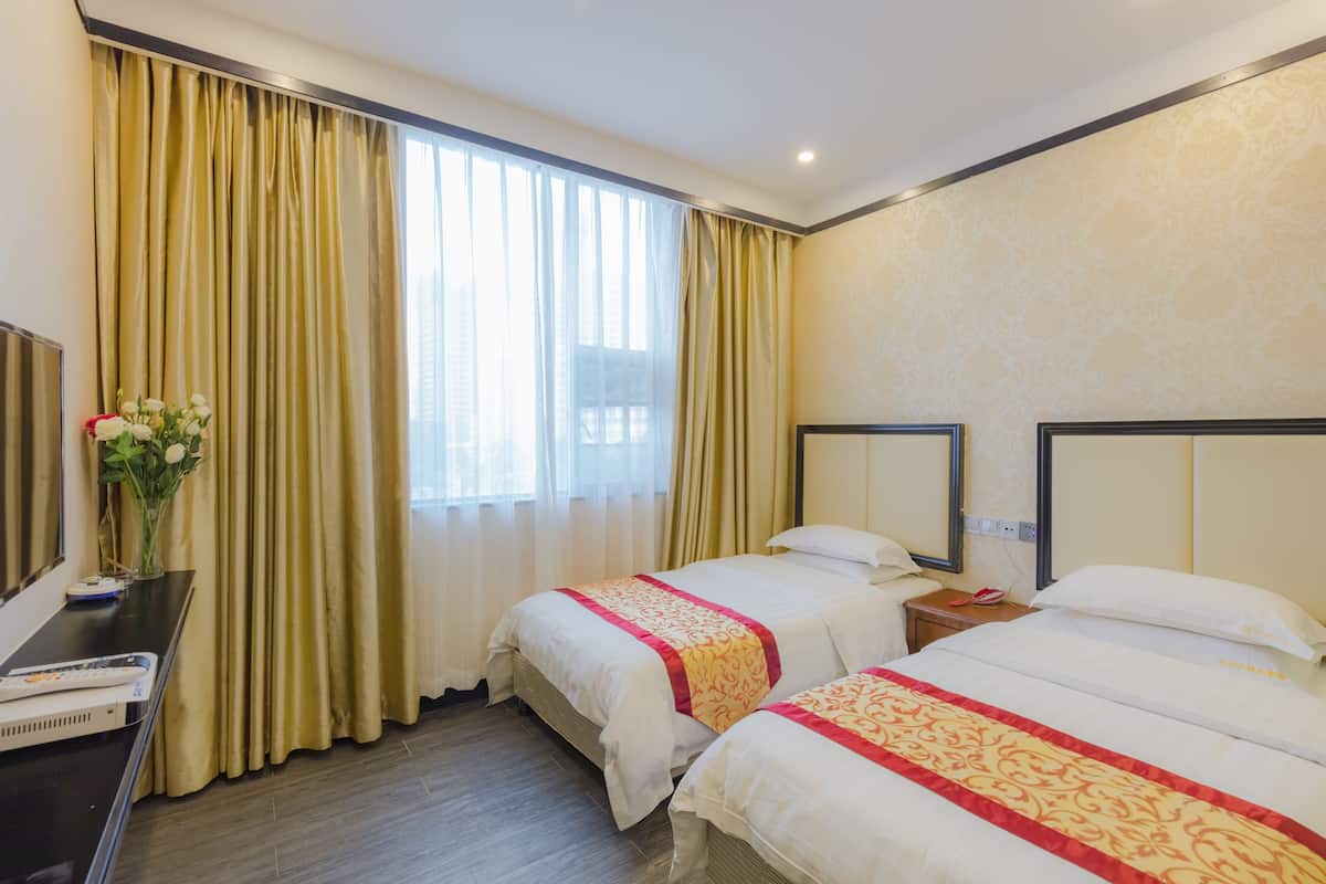 Ein Hotelzimmer mit zwei Betten, einem Schreibtisch und einem großen Fenster mit Vorhängen.