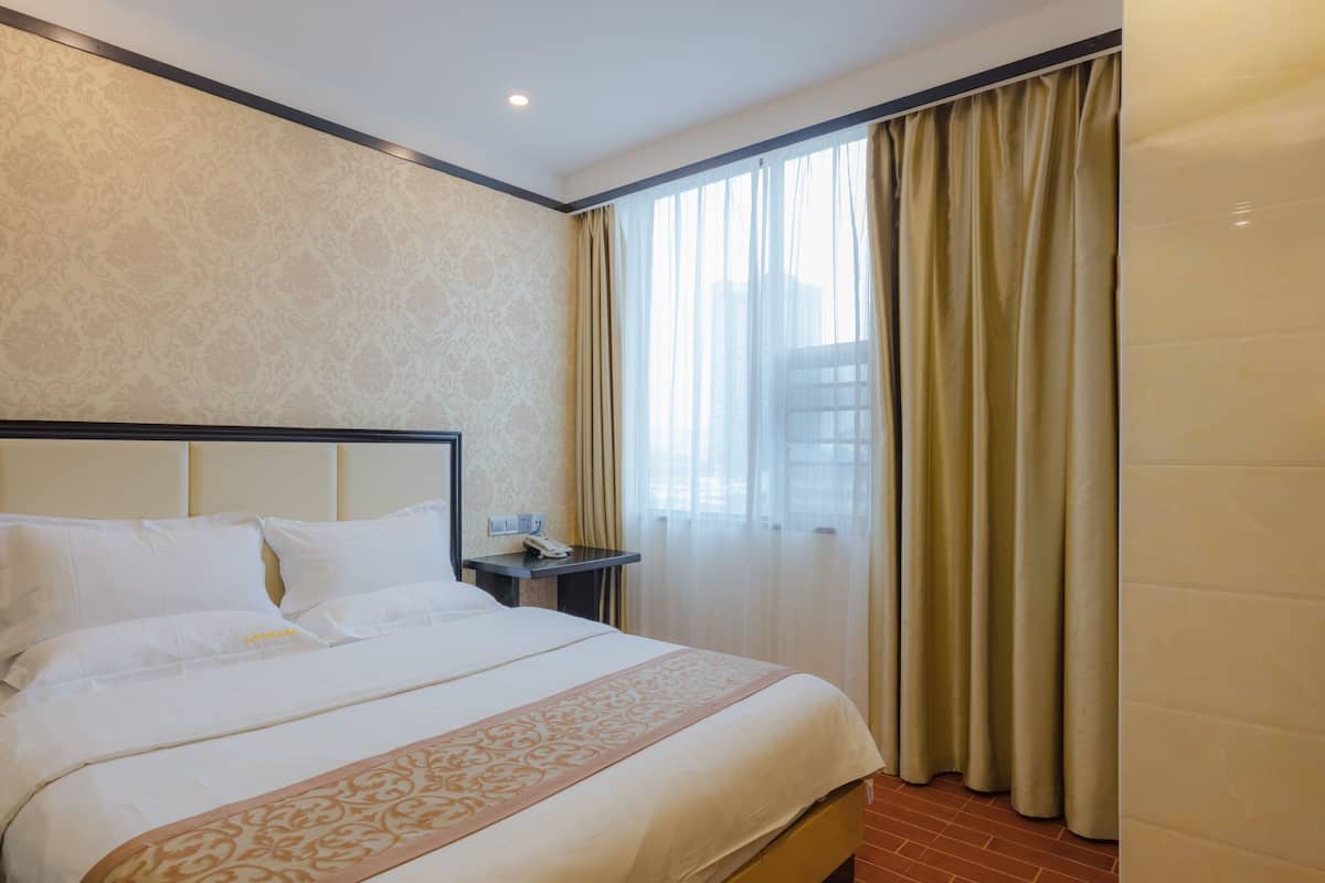 Ein Hotelzimmer mit einem großen Bett, einem Nachttisch mit Telefon und einem Fenster mit Vorhängen.