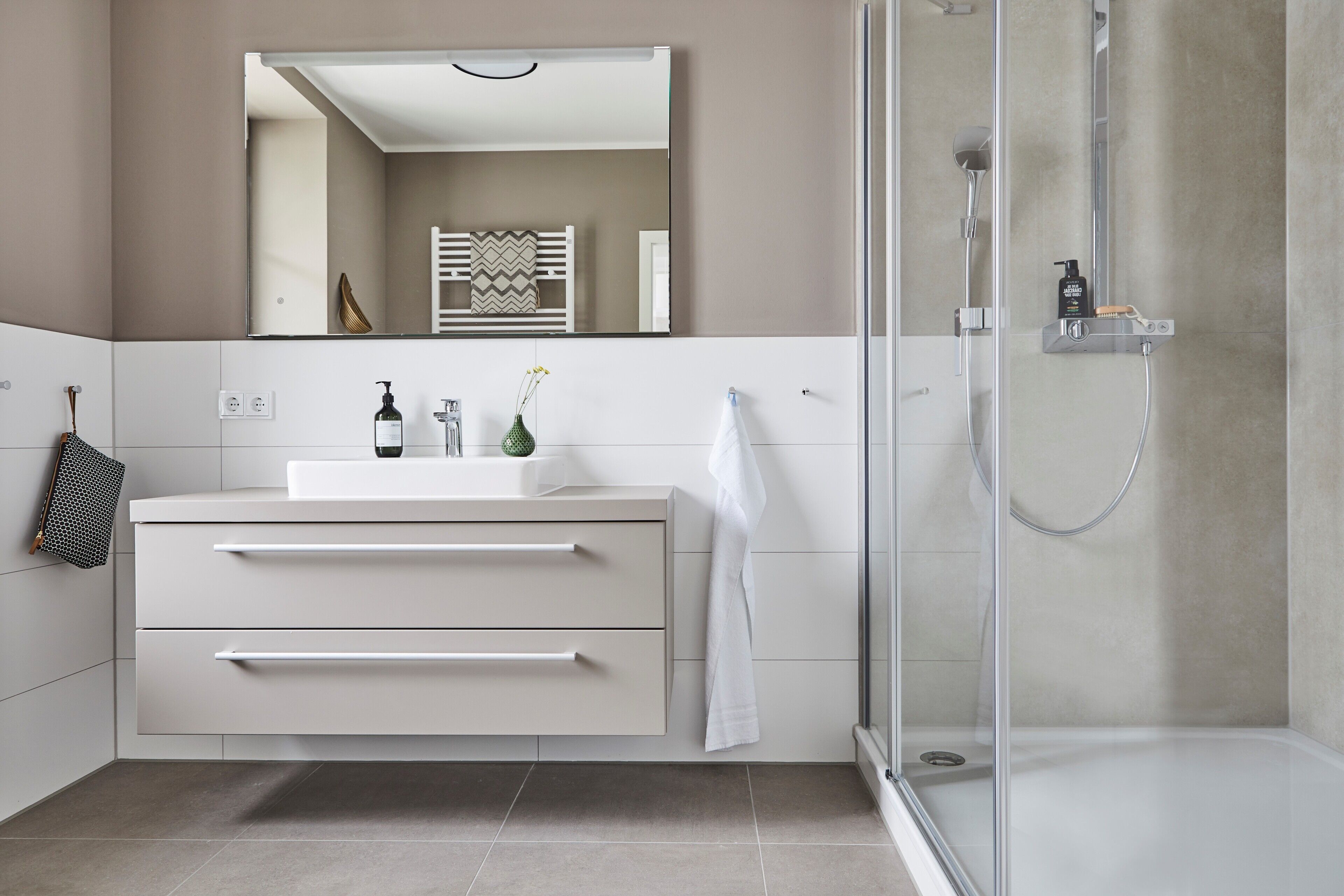 A modern bathroom with a glass shower enclosure, a white vanity with drawers, a mirror, and a towel rack.