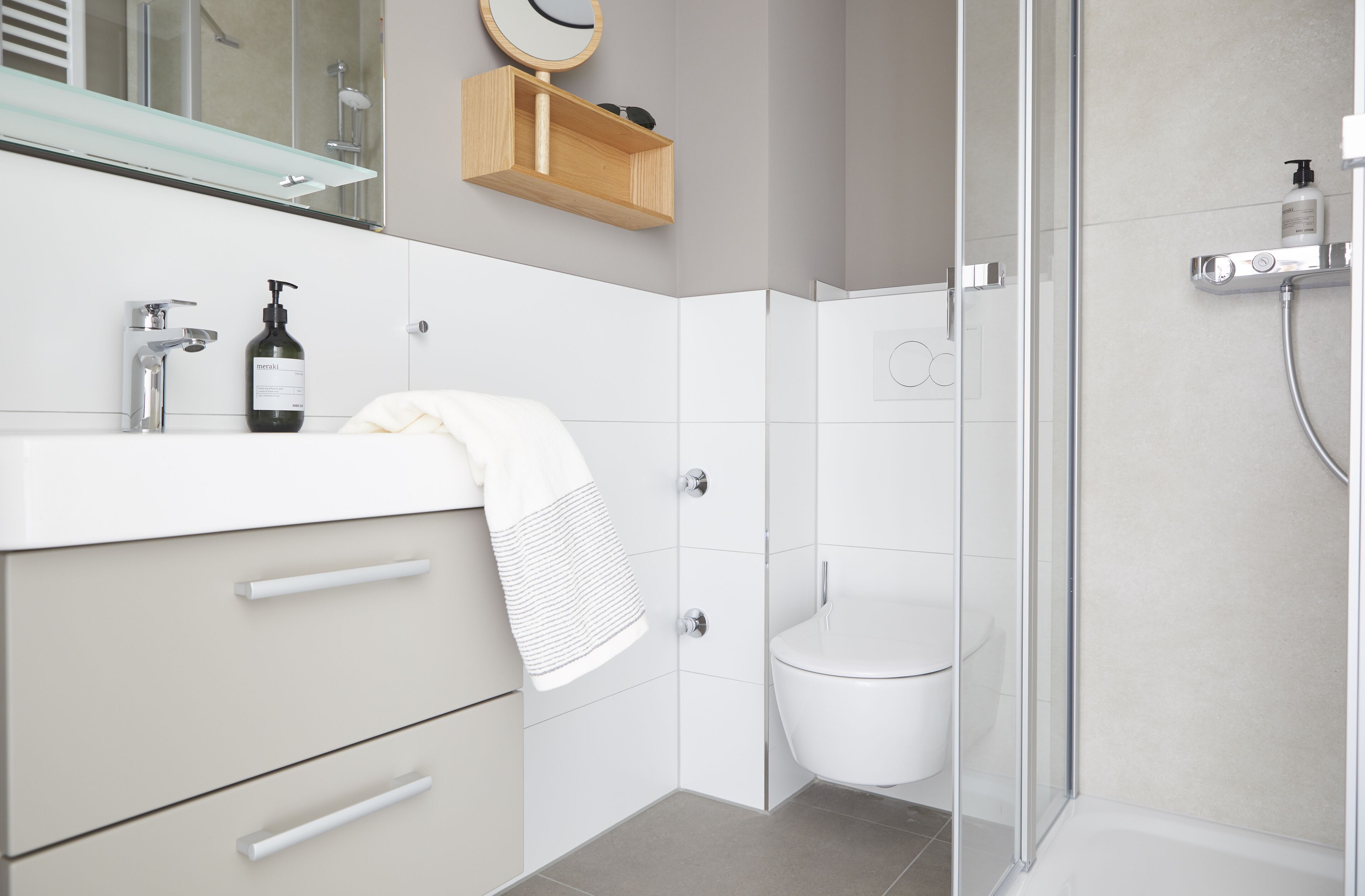 Un bagno moderno con box doccia in vetro, lavandino bianco e pensile in legno.