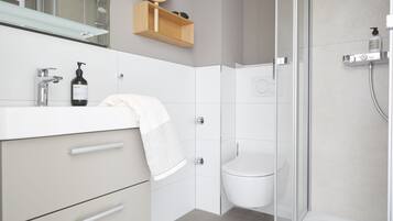 Un bagno moderno con box doccia in vetro, lavandino bianco e pensile in legno.