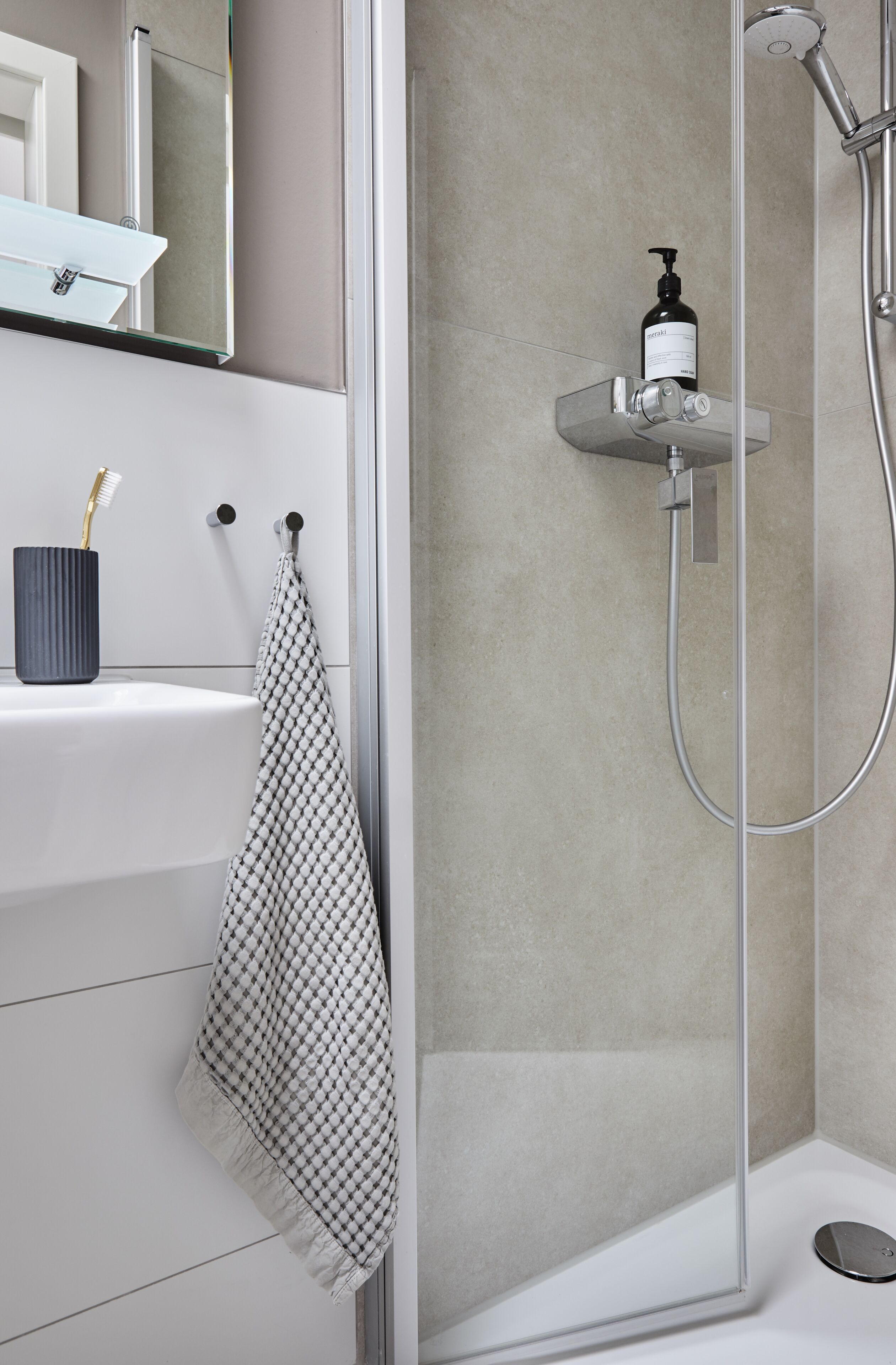 A modern bathroom with a glass-enclosed shower, a white sink with a toothbrush holder, and a towel rack.