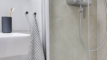A modern bathroom with a glass-enclosed shower, a white sink with a toothbrush holder, and a towel rack.