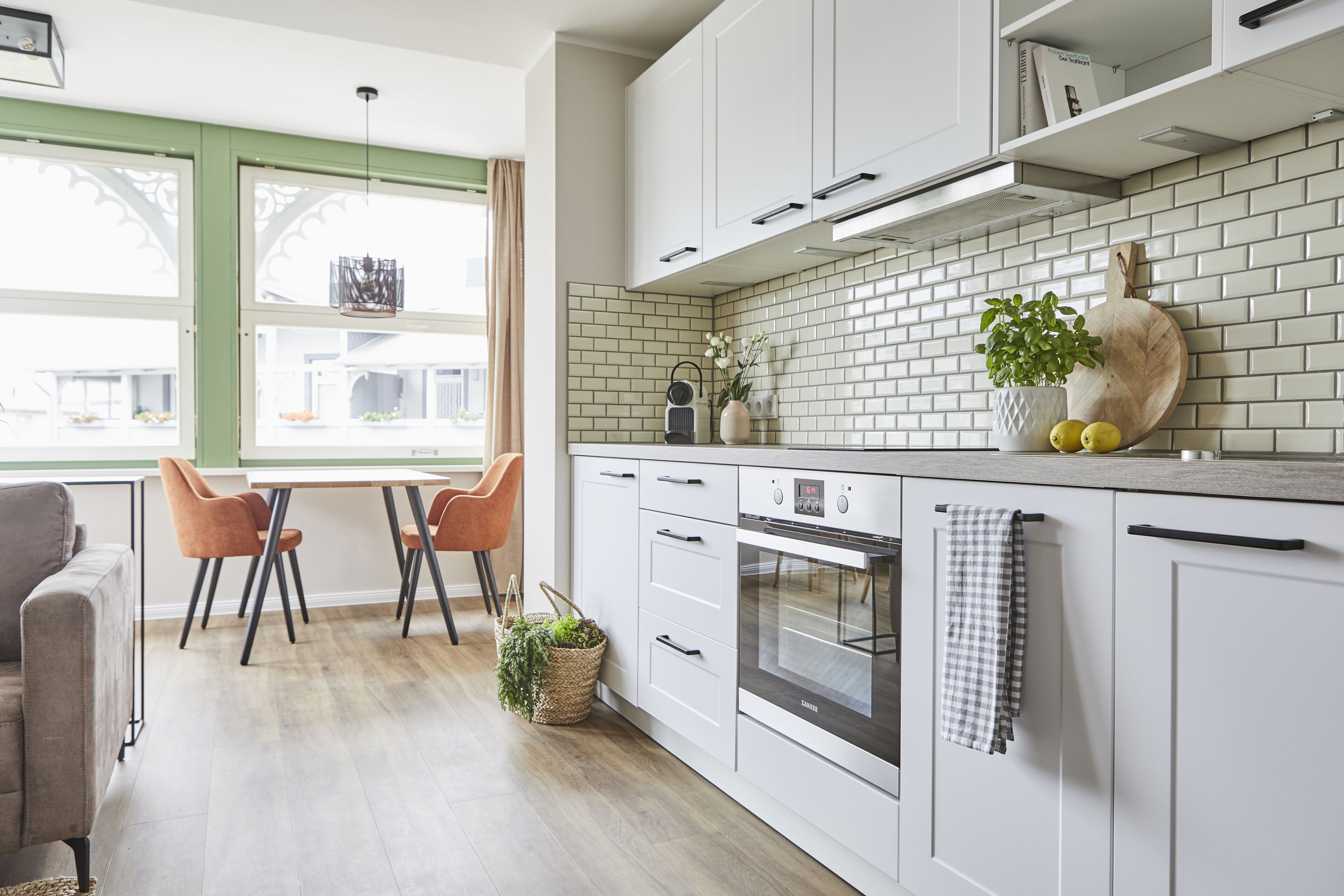 A modern kitchen with white cabinets, a built-in oven, and a window with green frames.