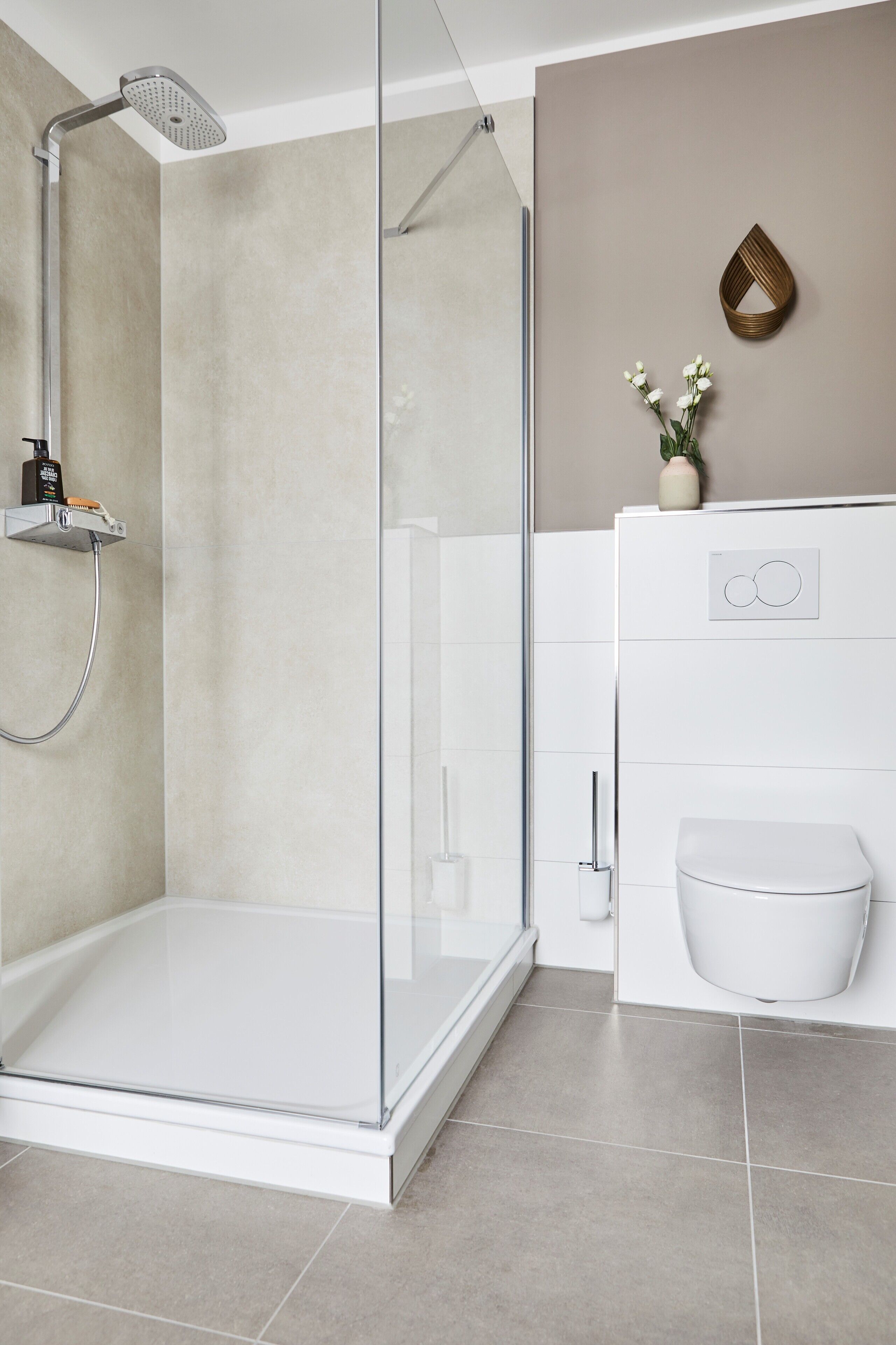 Un baño moderno con ducha envuelta en vidrio, un inodoro blanco y una pared color beige con un jarrón decorativo.