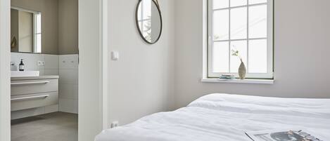 A bedroom with a large window, a bed, a bedside table, and a mirror.