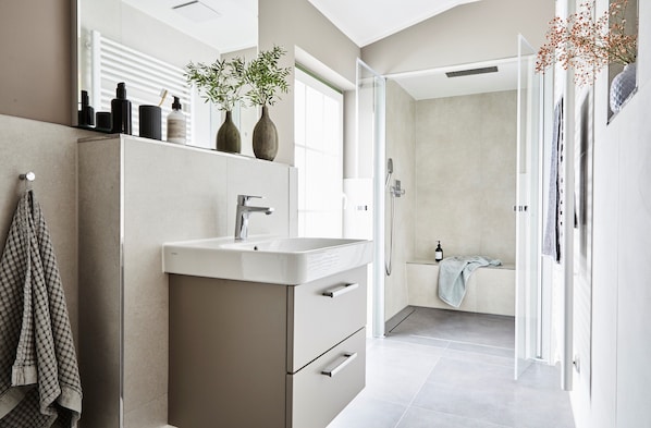 A modern bathroom with a large mirror, a sink, and a shower area. - Villa Fortuna (Sellin)