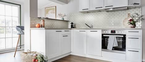 Een moderne keuken met witte kastjes, een betegelde spatwand en een ingebouwde oven.
