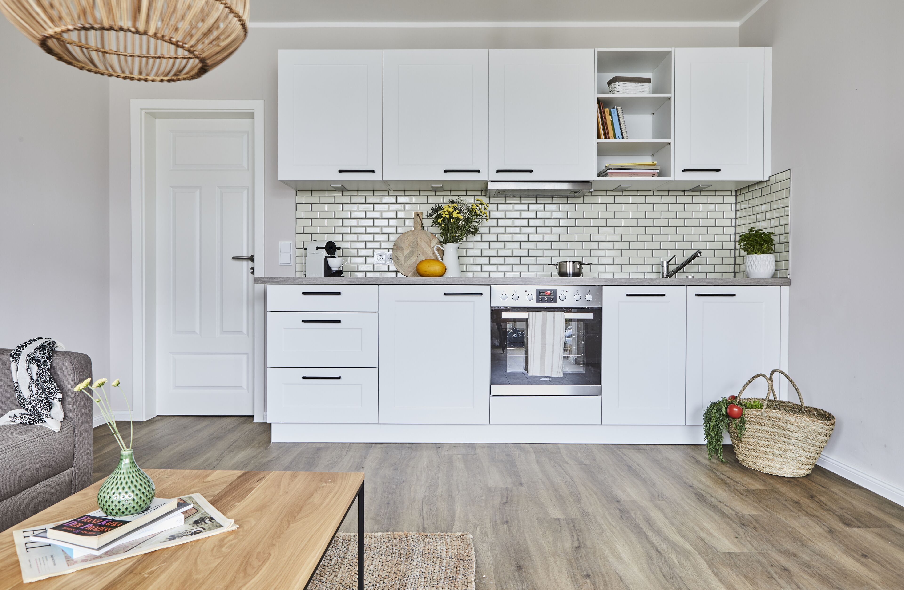 Una cocina moderna con armarios blancos, horno empotrado y salpicadero de azulejos tipo metro blancos.