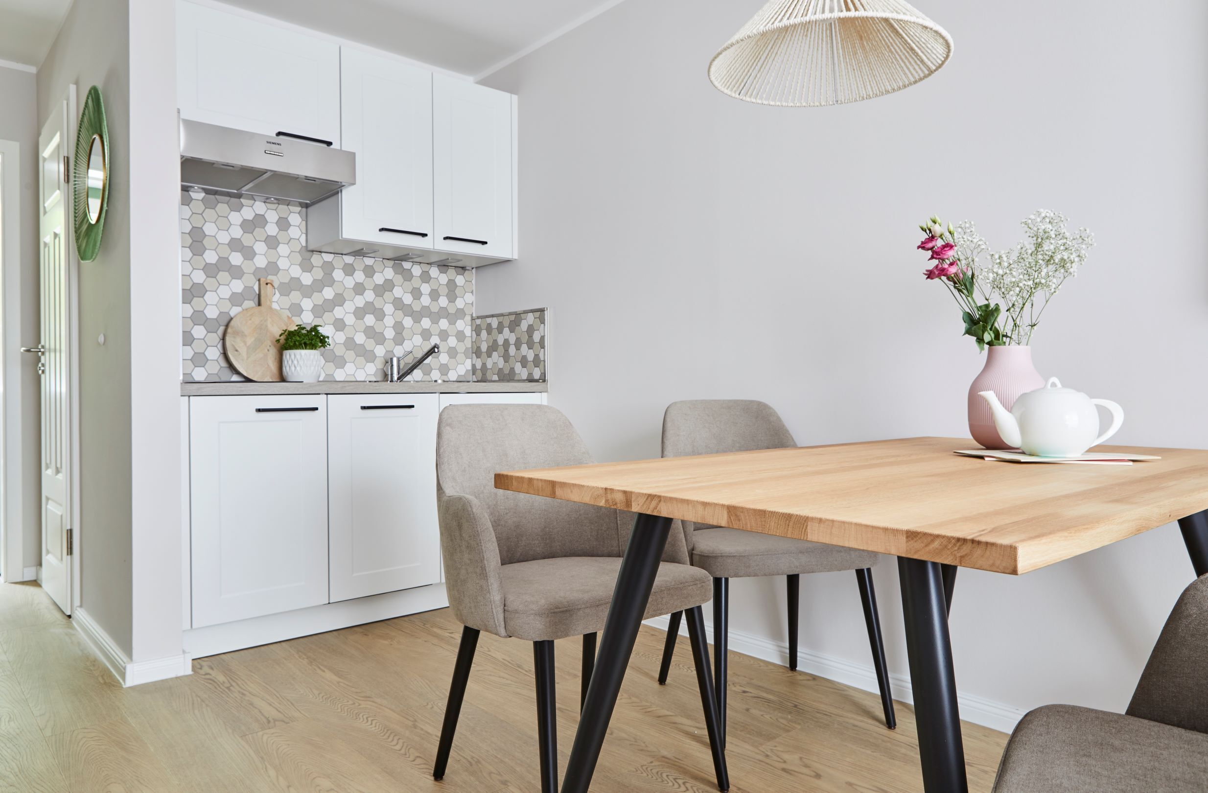 Una cocina moderna con armarios blancos, una mesa de comedor de madera y un jarrón con flores.