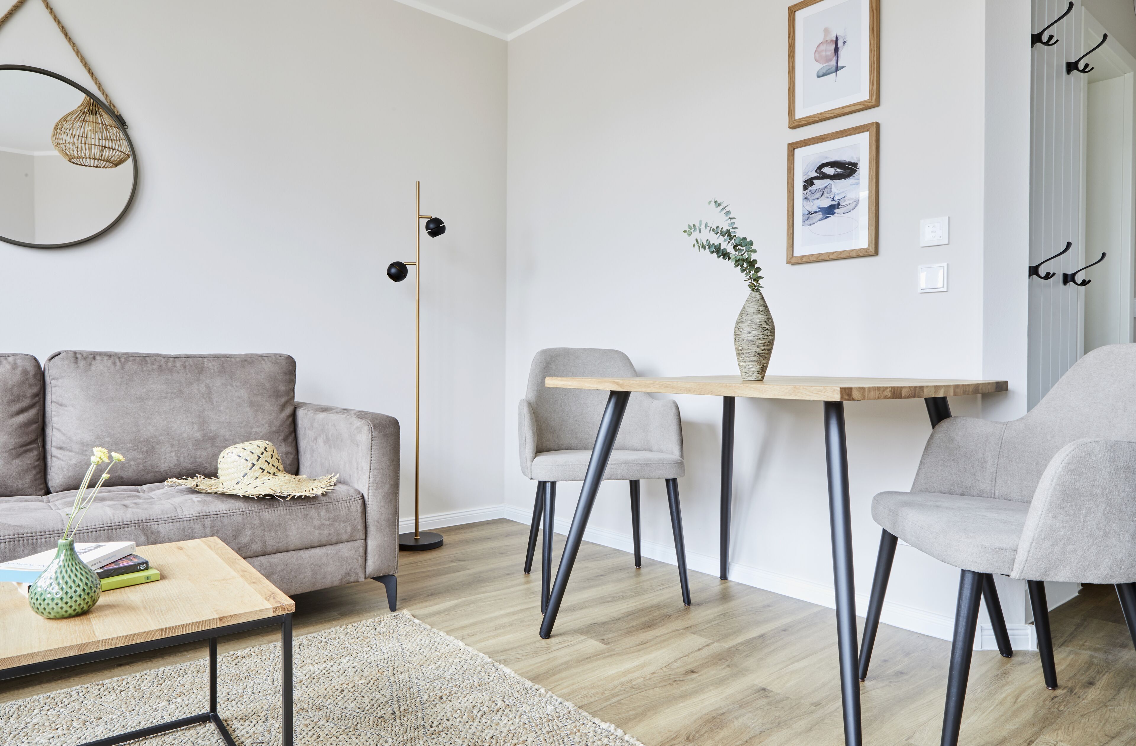 A modern living room with a grey sofa, a wooden coffee table, and a dining table with chairs.