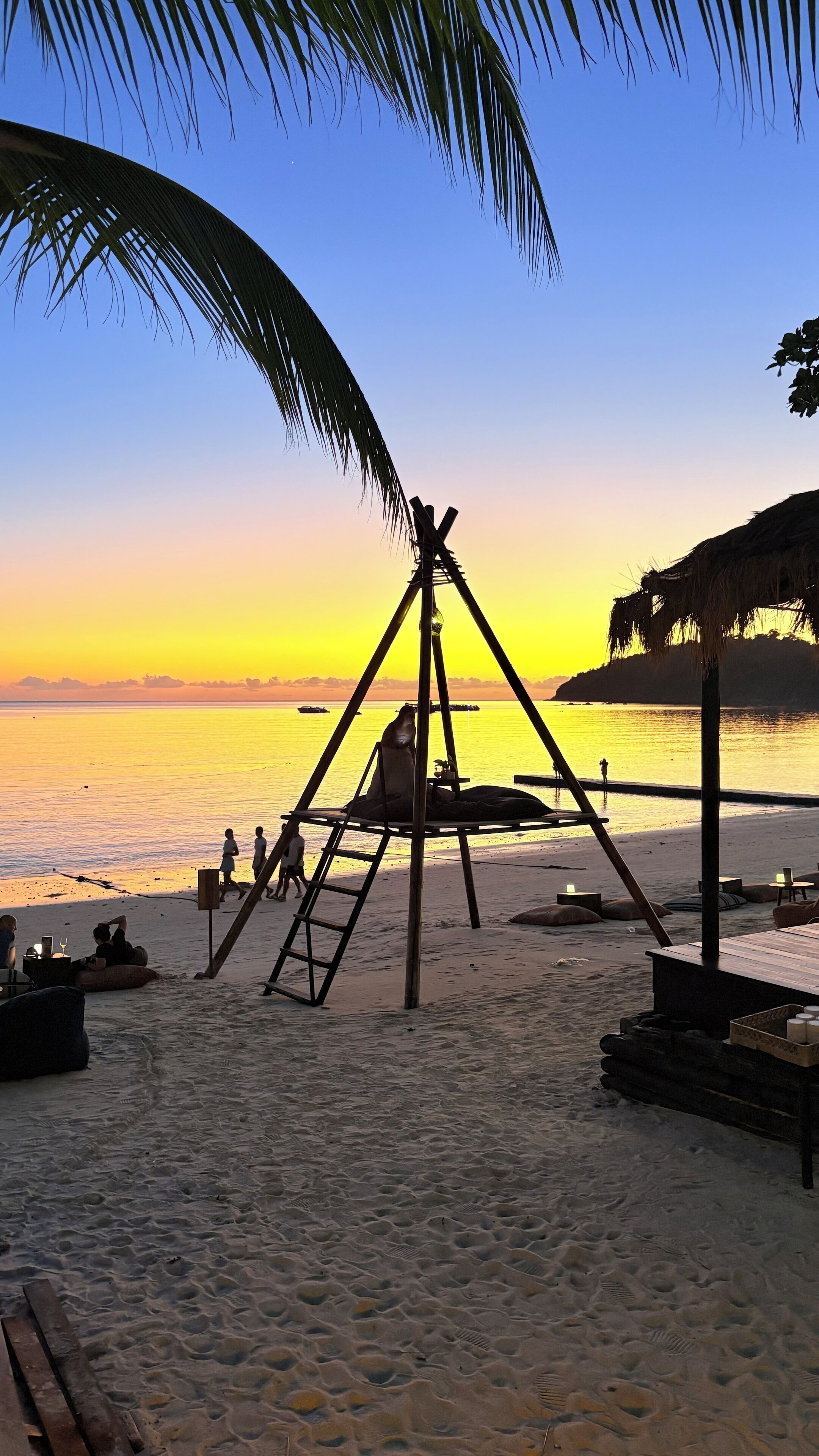 Eine Strandlandschaft mit Schaukeln, Palmen und einem Sonnenuntergang über dem Wasser.
