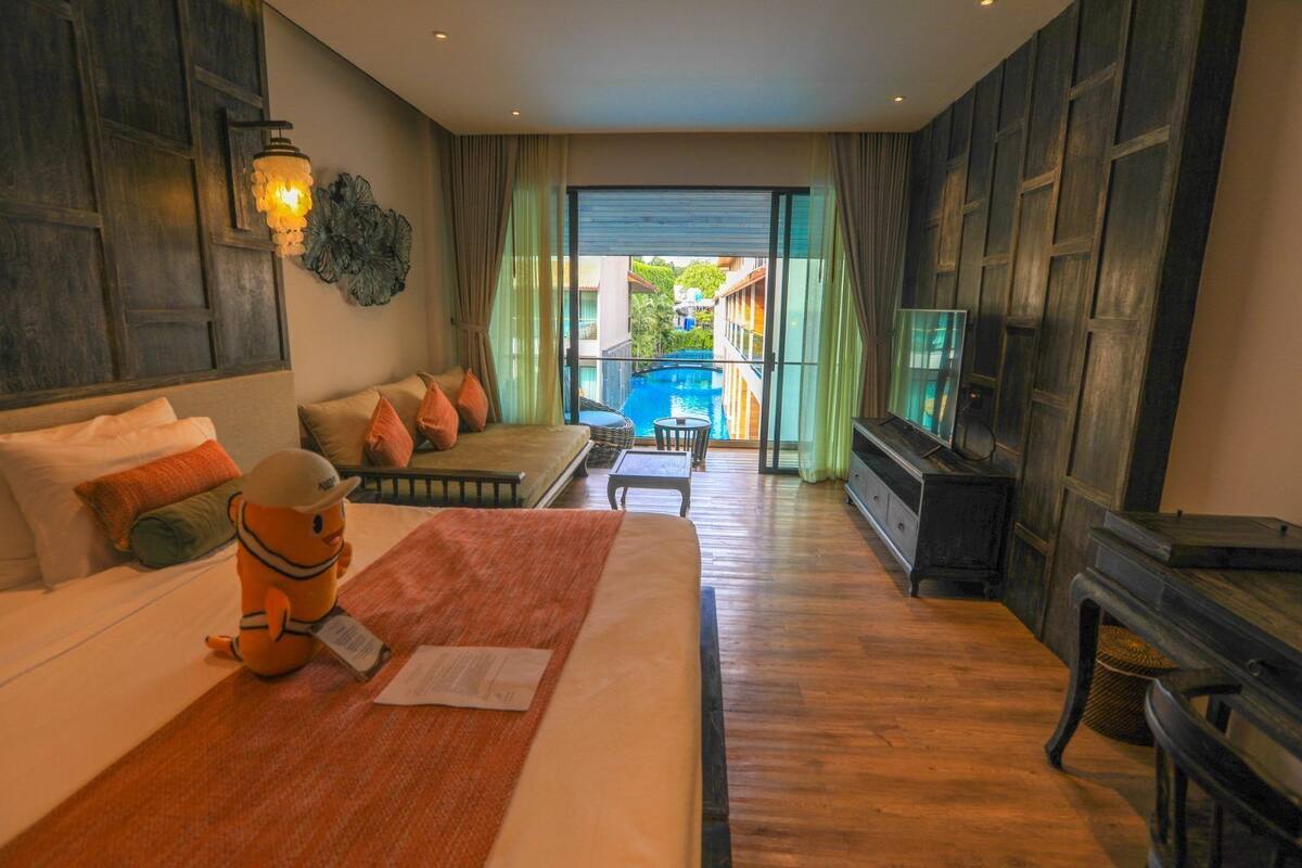 A hotel room with a bed, a sofa, a TV, a piano, and a view of a swimming pool.