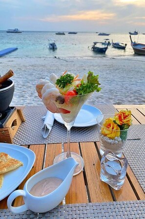 Mesa servida con una ensalada de mariscos, un vaso de agua y una jarra pequeña, con barcos al fondo.
