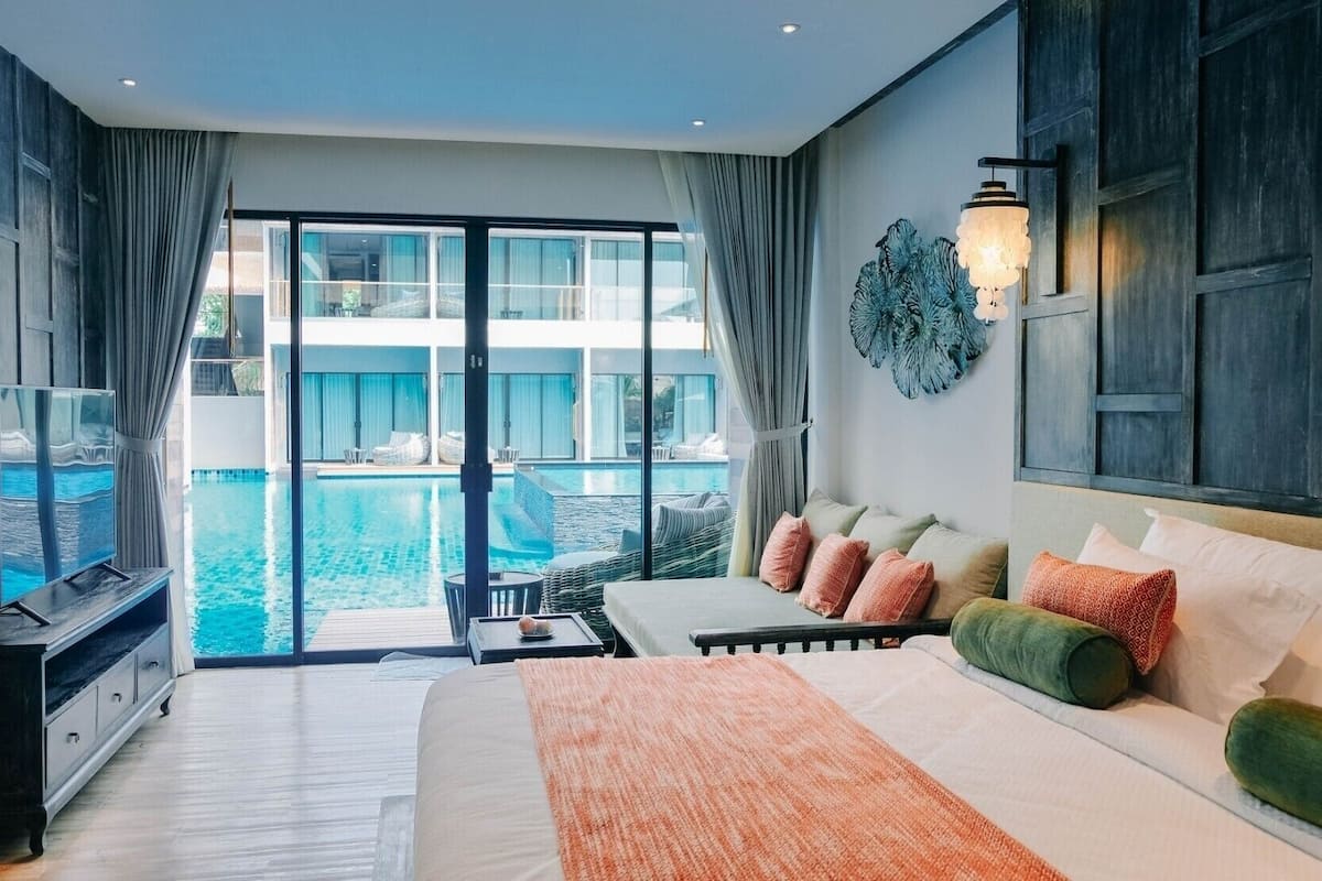 A bedroom with a large bed, a TV, a pool view, and a balcony.