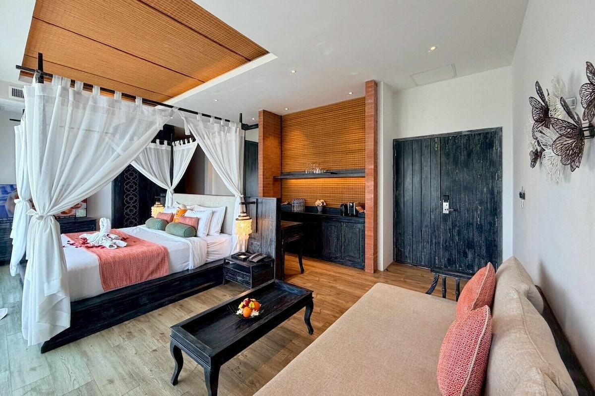 A bedroom with a canopy bed, a sitting area with a sofa and a coffee table, and a kitchen area with a counter and cabinets.