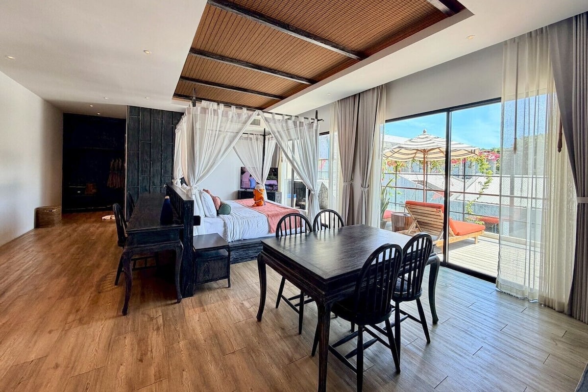 A spacious room with a large dining table, a cozy seating area, and a balcony with a view.