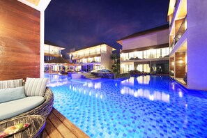 Un hotel moderno con piscina, mobiliario exterior y balcones bien iluminados.