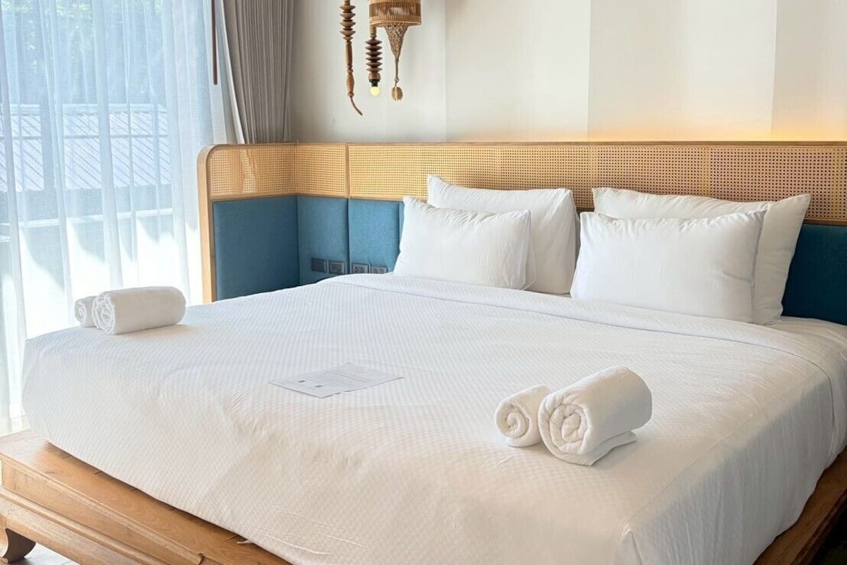 A large bed with white linens, a wooden headboard, and a hanging light fixture.