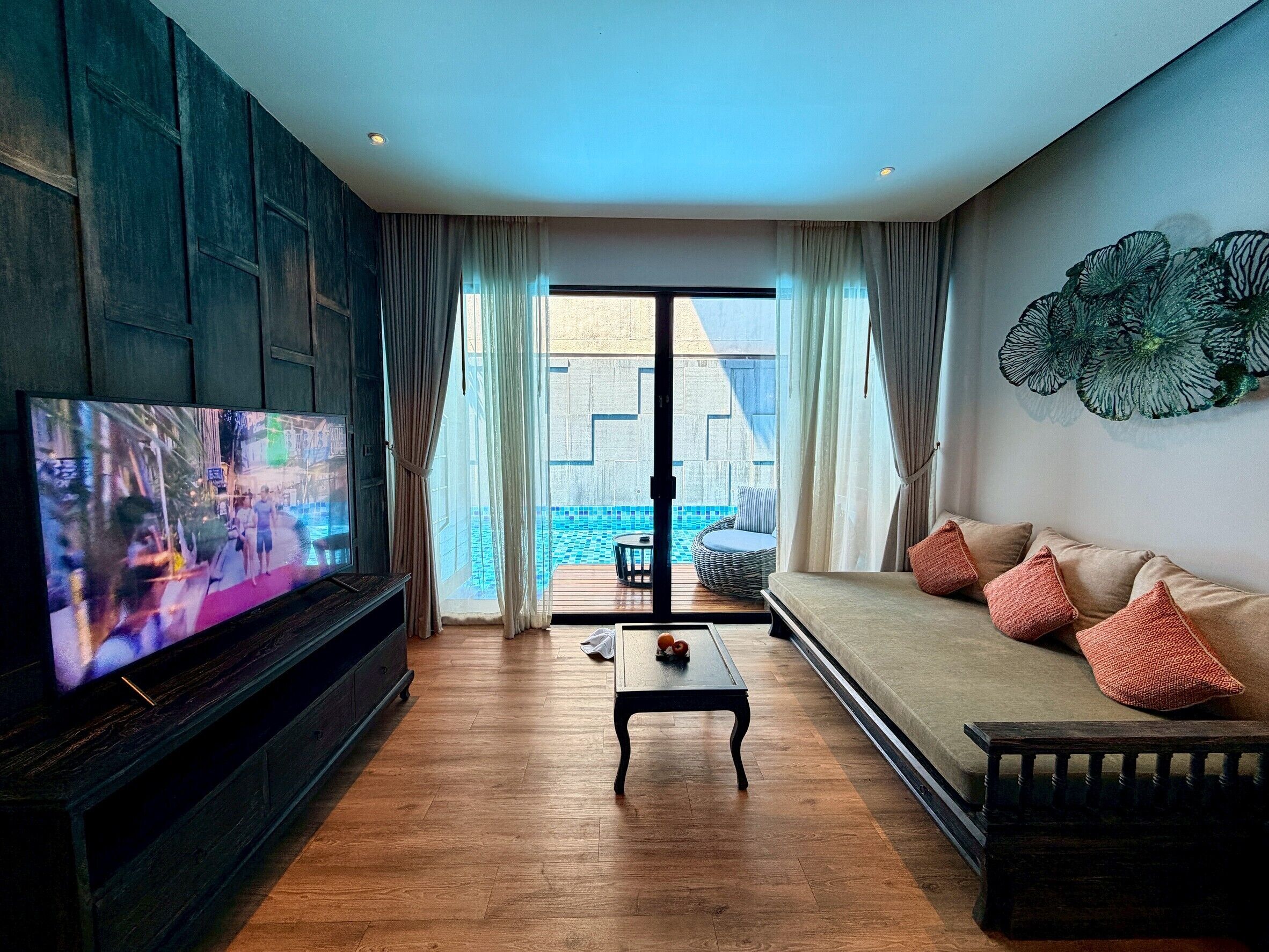 A living room with a TV, a sofa, a coffee table, and a view of a pool.
